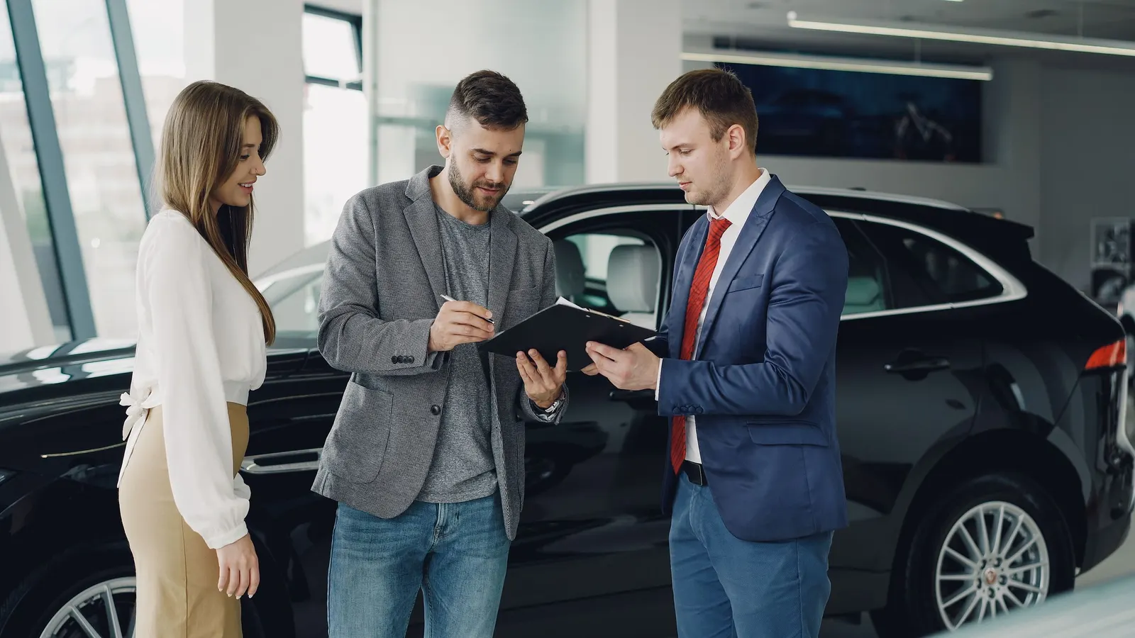 A couple going over paperwork with a salesman beside a car in a dealership
