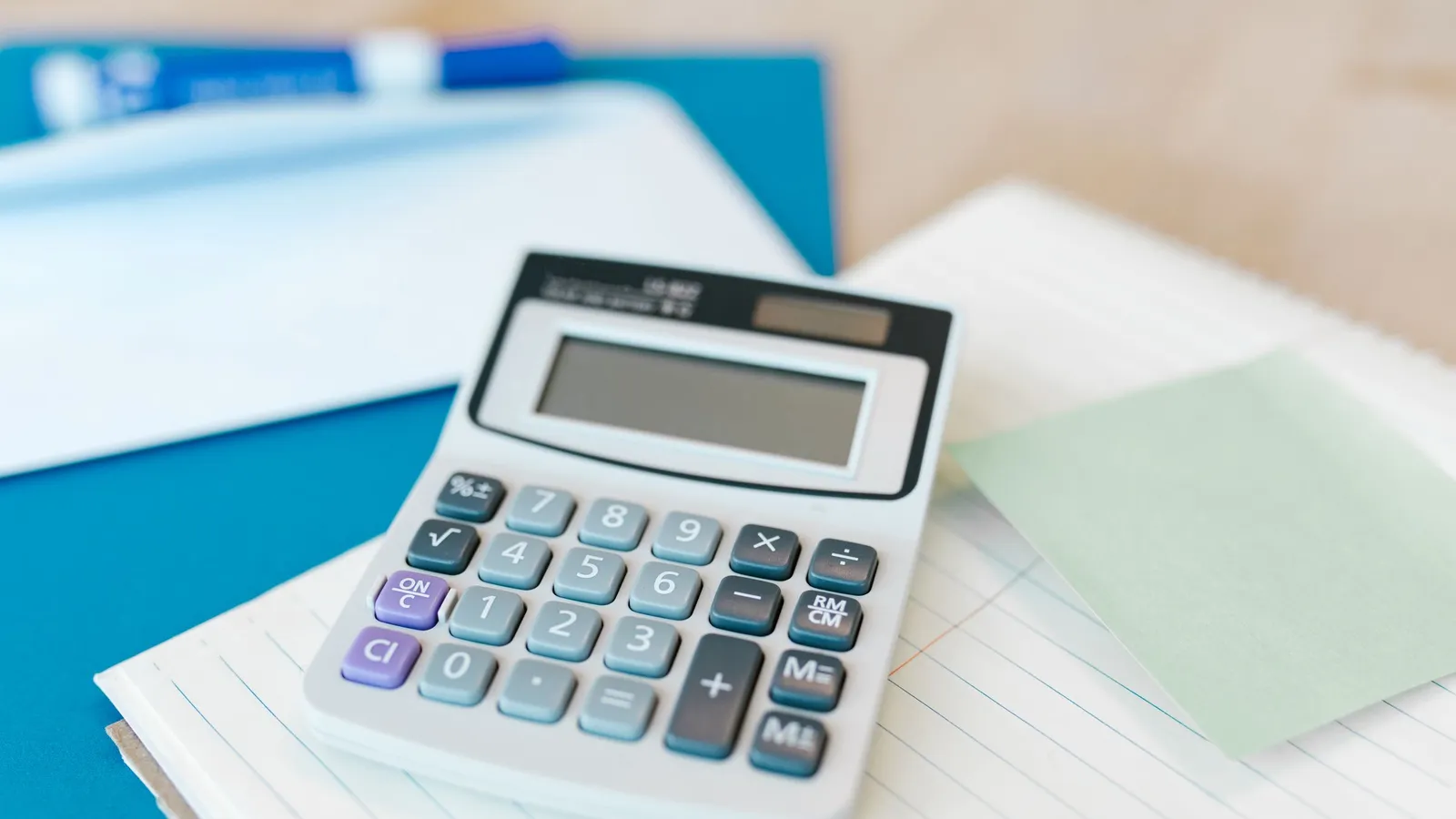 A calculator on a notepad beside a blue folder